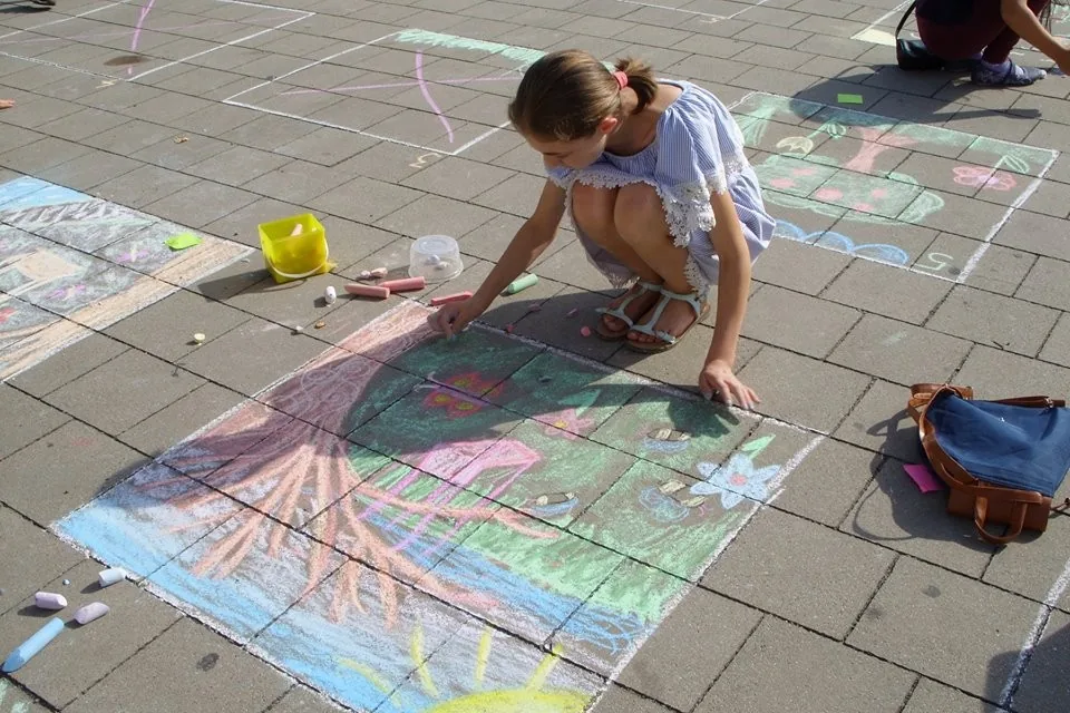 Žiačka kreslí kriedou na dlažbu námestia